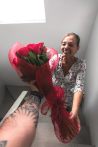 Tatooed arm giving roses to smiling woman.